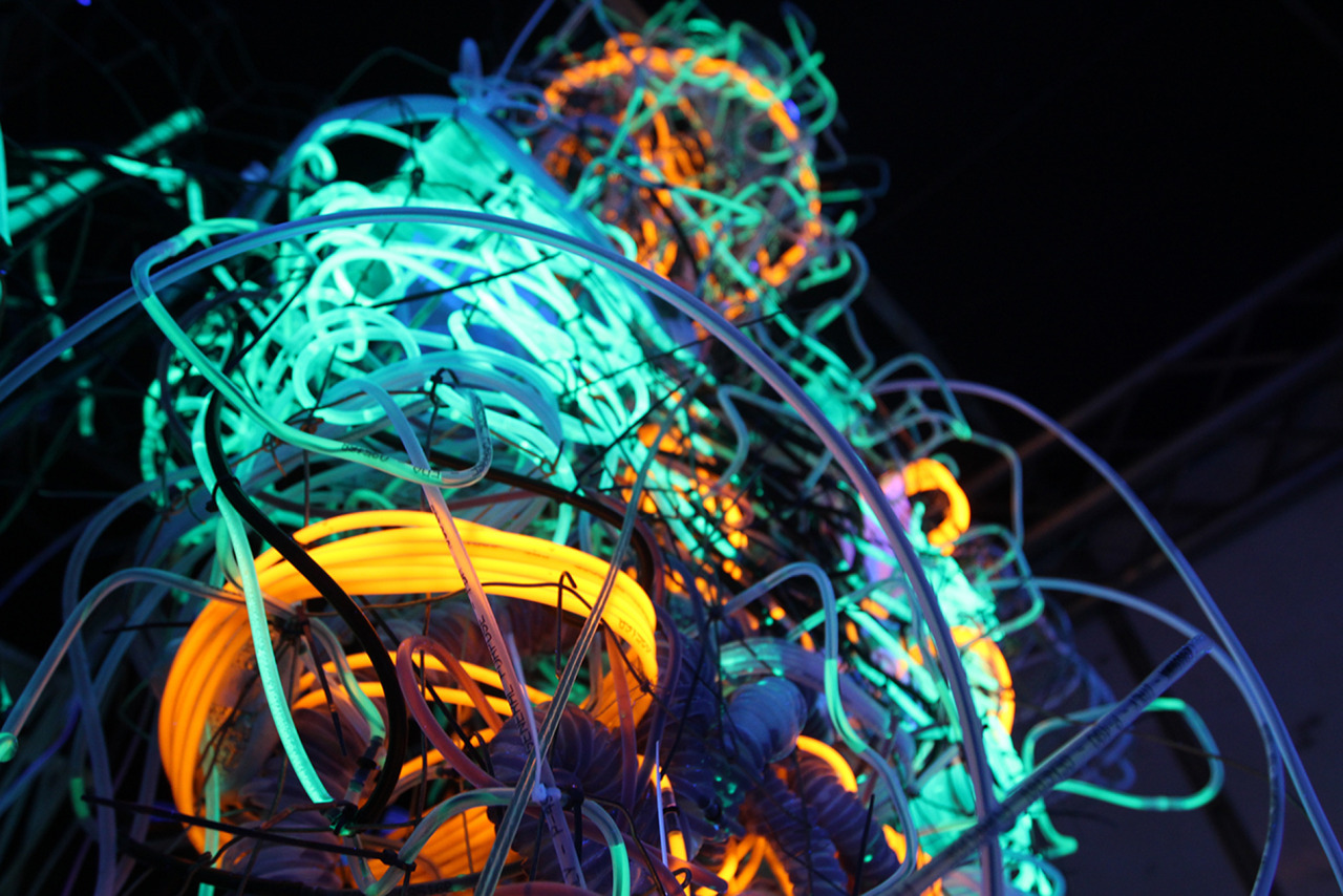 Close-up of woven PVC tubing glowing green and orange under UV light.