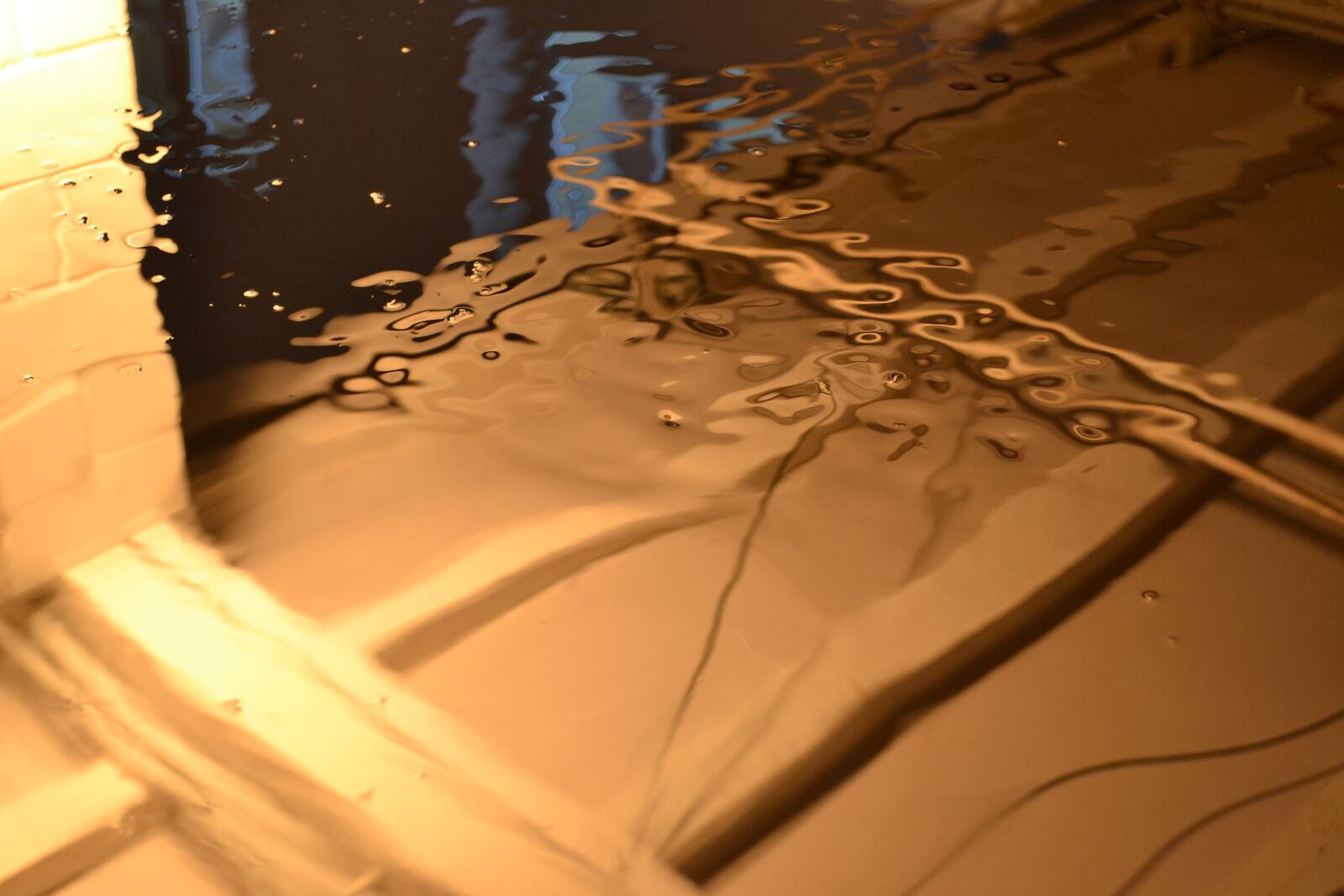 Close-up of ferrofluid rippling across the tank under warm light.